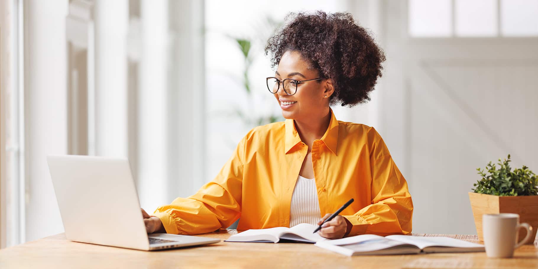 A young woman working at a desk while looking at a laptop.