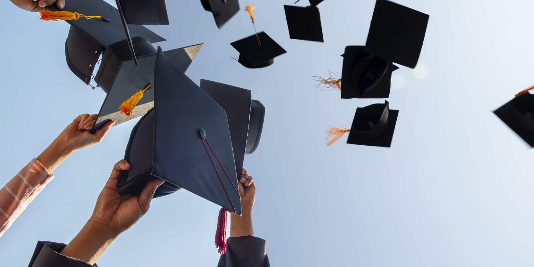 Graduation caps in the air against a blue sky.