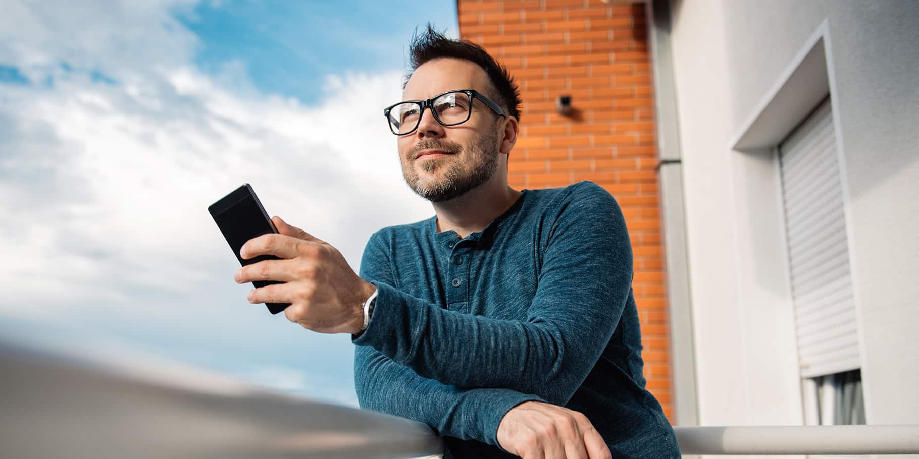 A smiling man dressed in casual attire holding a smartphone.